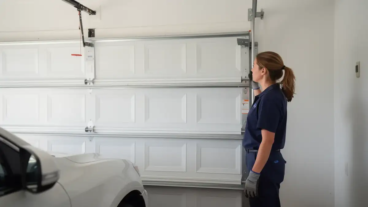 A technician in a blue uniform is inspecting a white garage door.